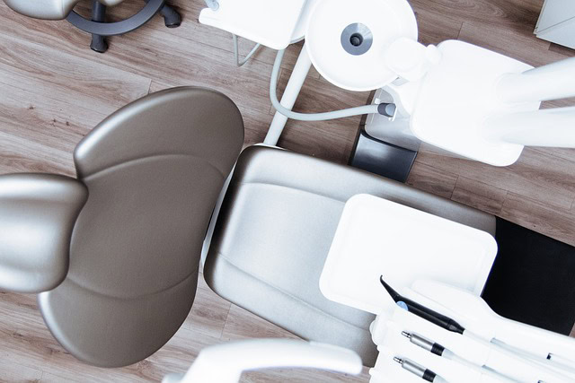 Overhead view of a dentist's chair with surrounding dental equipment on a wooden floor.